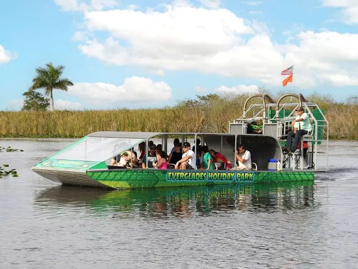 Everglades airboat with tourists on a scenic waterway tour under a clear sky.