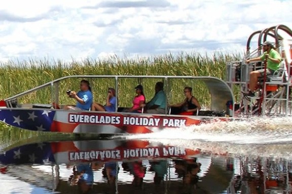 Airboat with passengers gliding through a wetland under a cloudy sky.