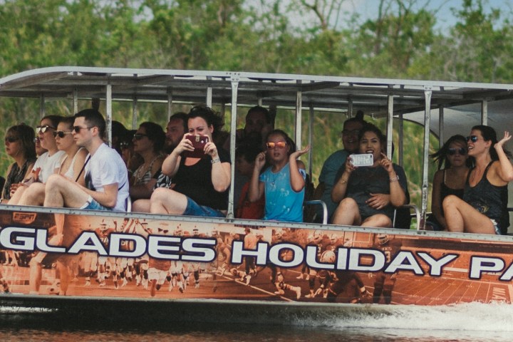 Tourists on an airboat in a swamp wearing casual clothing, some taking photos.