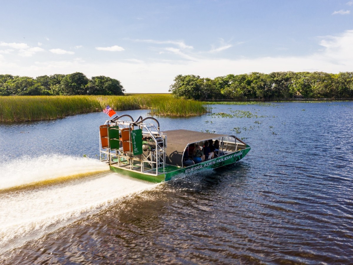 Airboat cruising on a wide lake with grassy banks and trees under a clear blue sky.