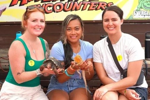 Three people sitting with reptiles at a zoo exhibit.