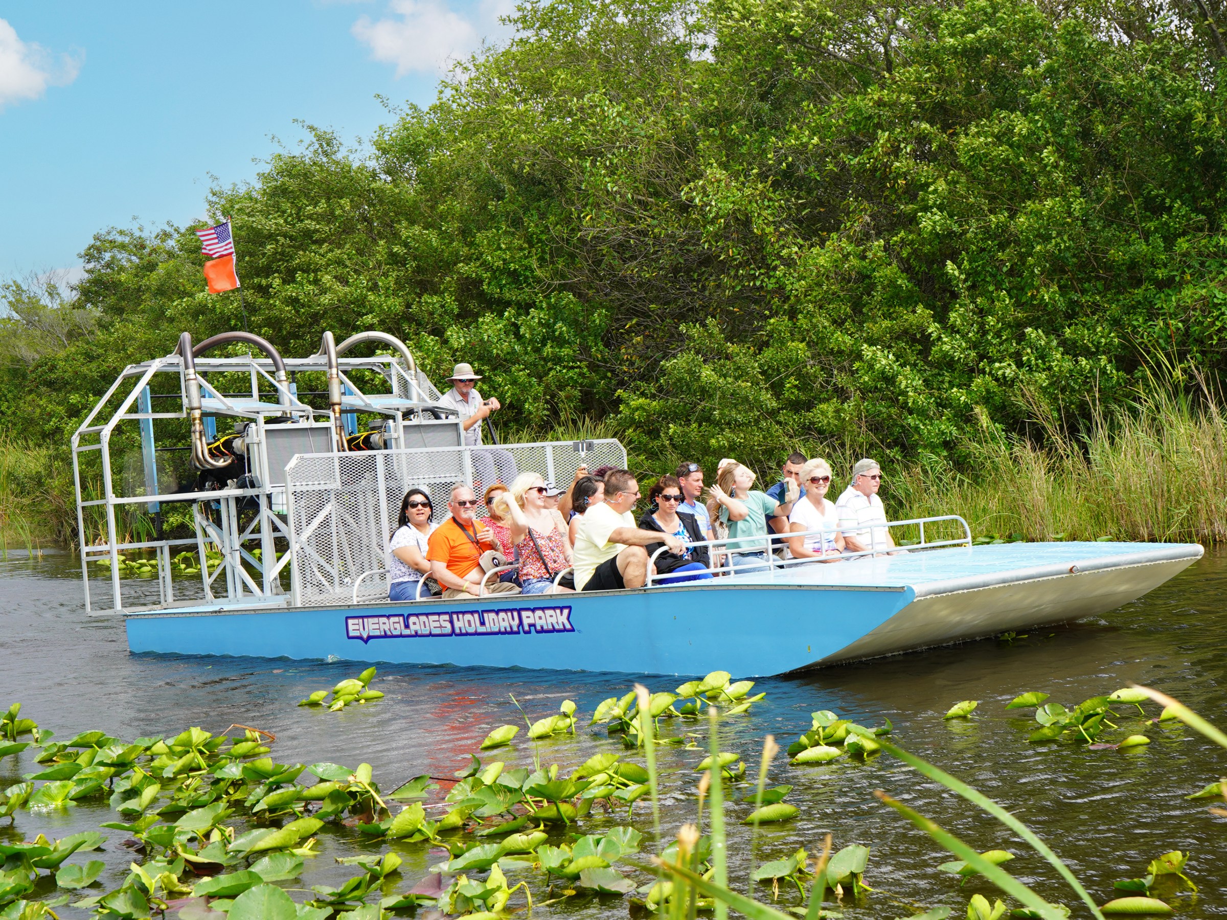 Airboat with people touring a lush, green waterway in sunny weather.