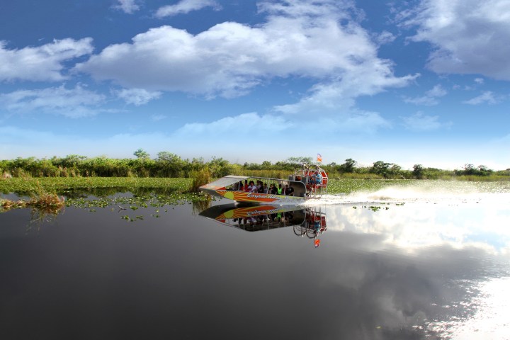 Airboat glides through a calm marsh under a partly cloudy sky.