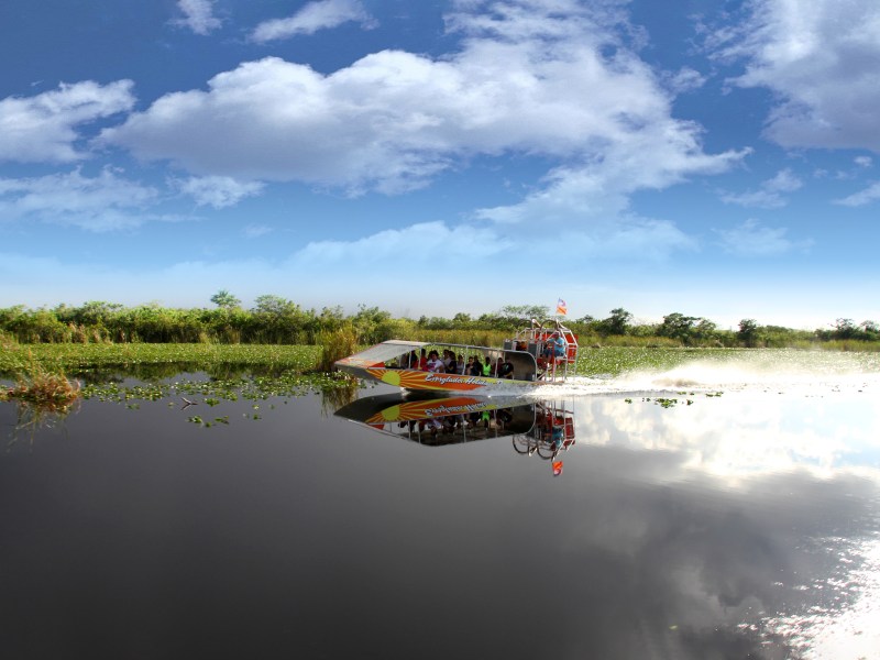 Airboat glides through a calm marsh under a partly cloudy sky.