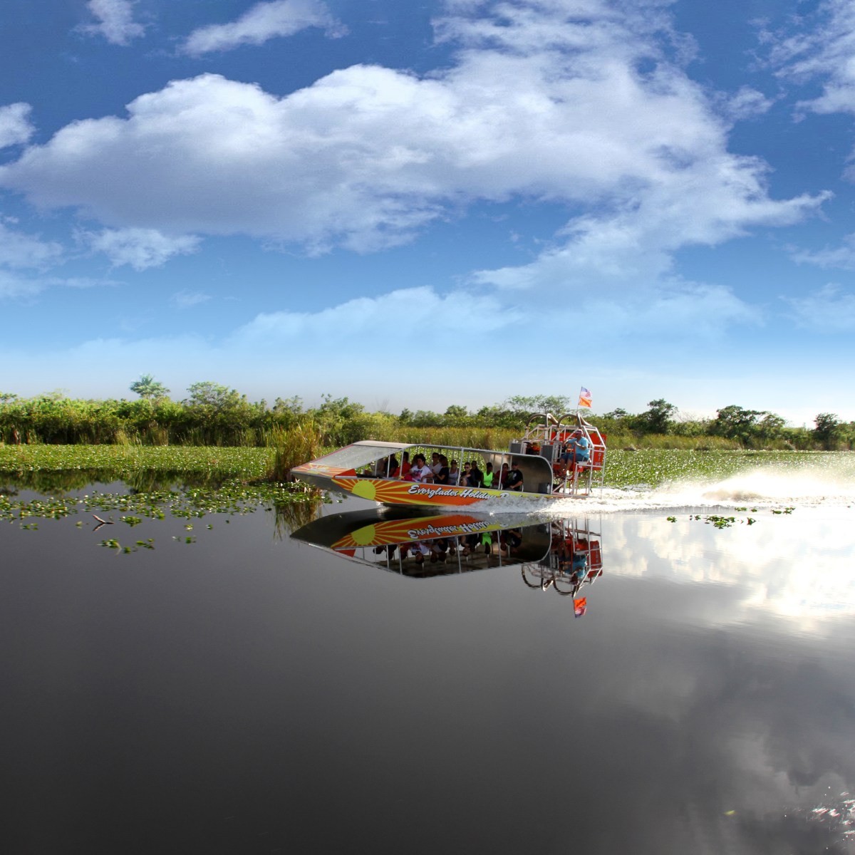 Airboat glides through a calm marsh under a partly cloudy sky.