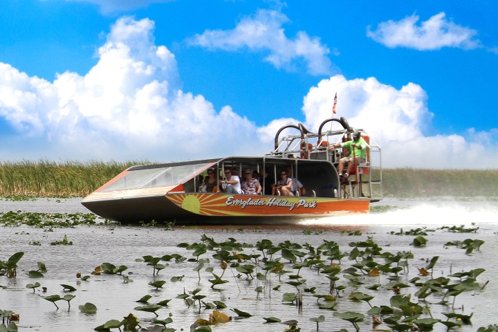 Airboat speeding through wetlands under a blue sky with clouds.