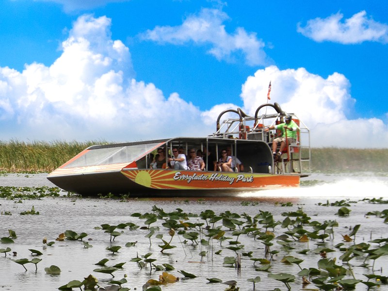 Airboat speeding through wetlands under a blue sky with clouds.