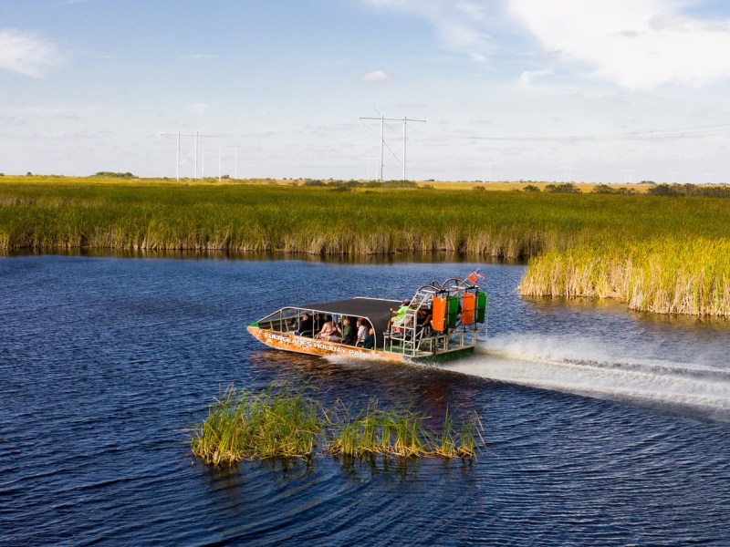 Airboat on a river surrounded by tall grass against a blue sky.