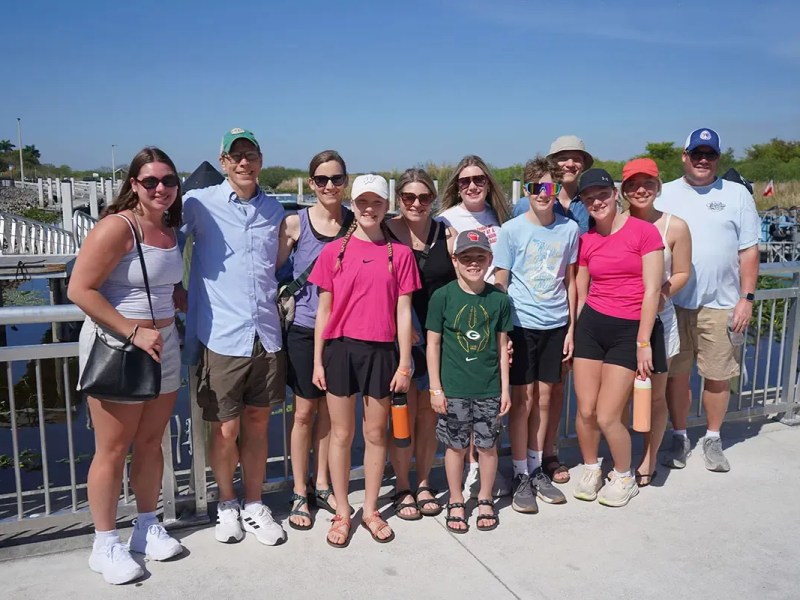 Group of people posing outdoors by a railing, with a clear blue sky.