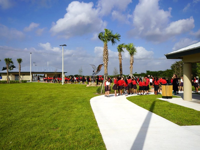 Group of people in red shirts outside, lined up on a walkway in a grassy area.