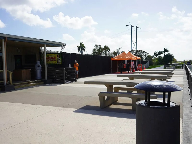 Outdoor area with picnic tables, an orange tent, and a gift shop under a partly cloudy sky.