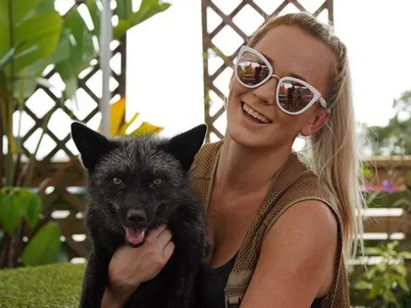 Woman with sunglasses holding a black fox in a garden setting.