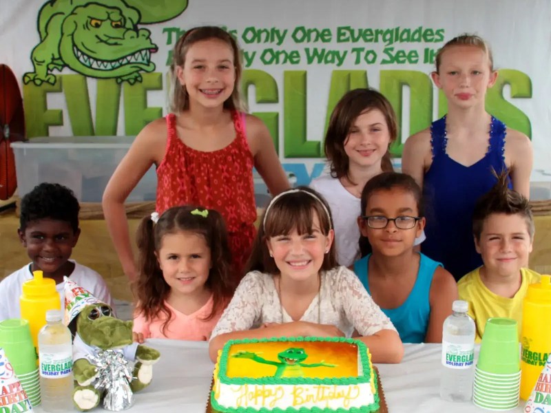 Group of children smiling around a birthday cake with an alligator design.