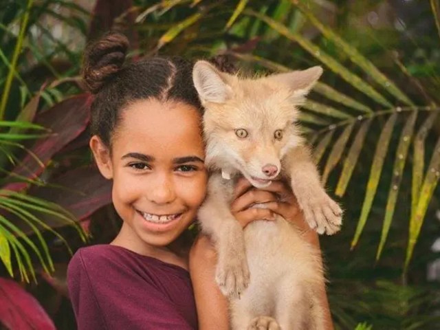 Child holding a small light-furred fox, surrounded by tropical foliage.