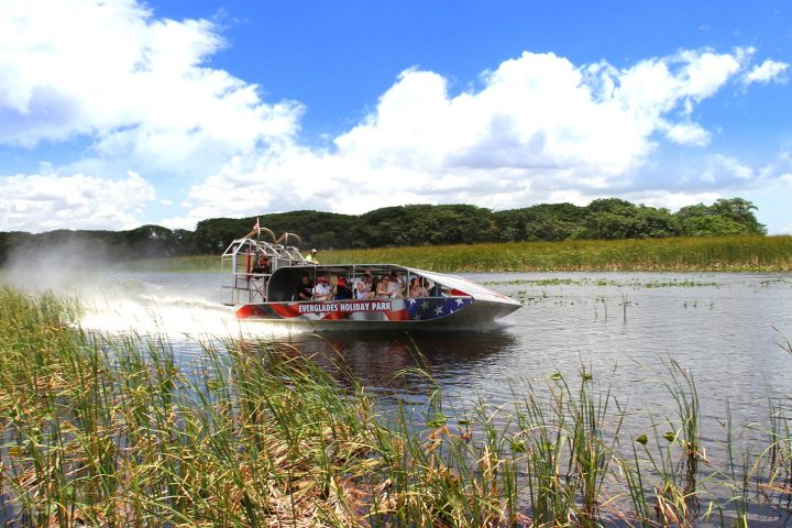 Airboat speeding through a grassy wetland under a partly cloudy sky.