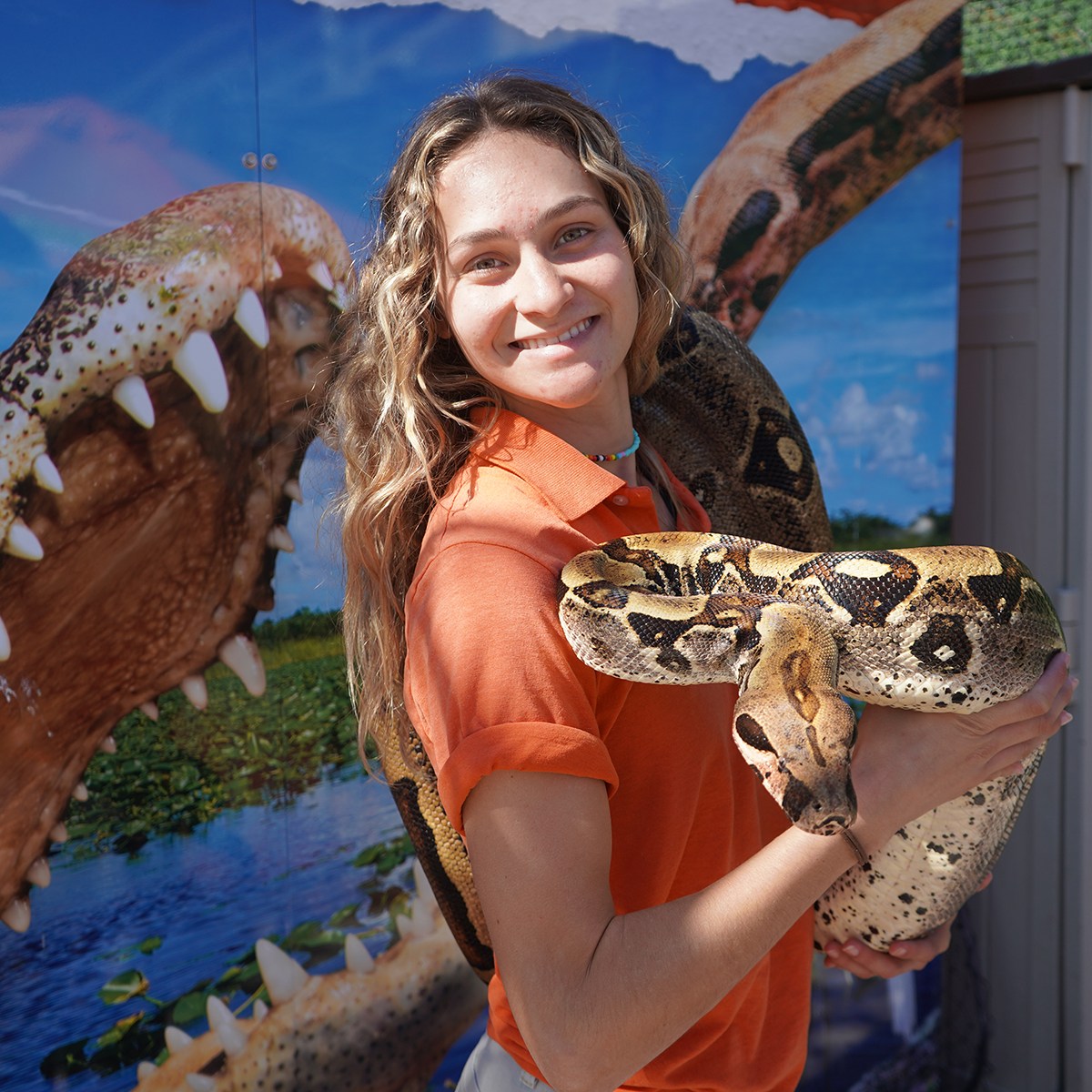 Person smiling with snake, standing by crocodile mural