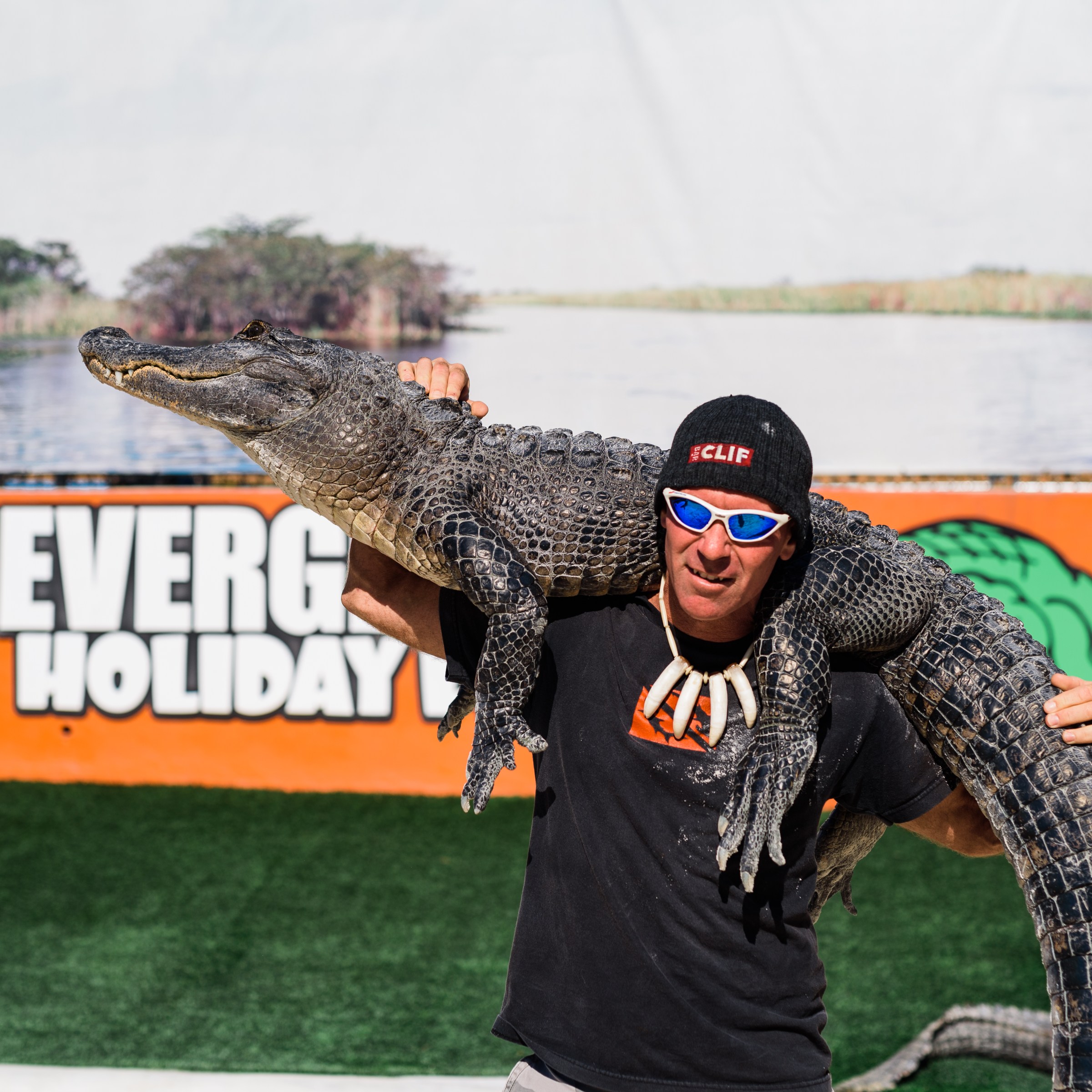 Person holding alligator on shoulder, standing in front of a sign.