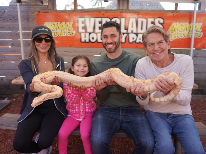 Four people holding a large snake, smiling at a wildlife park.