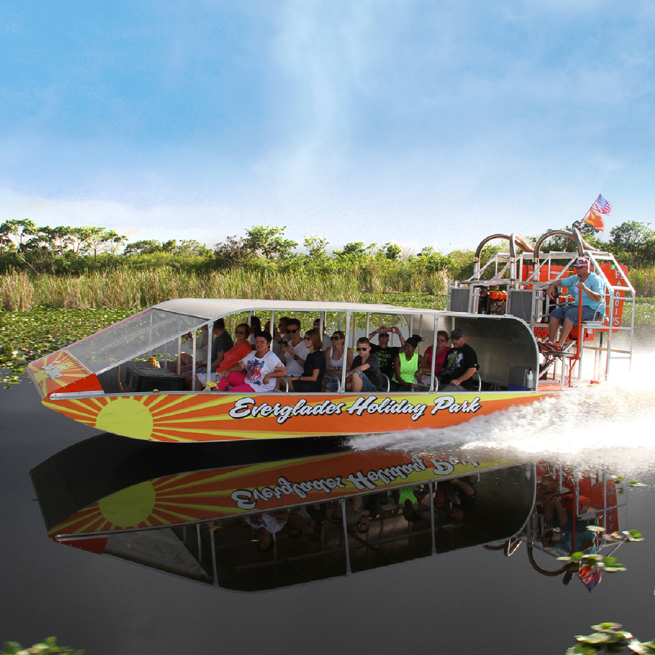 Airboat with passengers glides on a calm river in a grassy wetland under a clear blue sky.